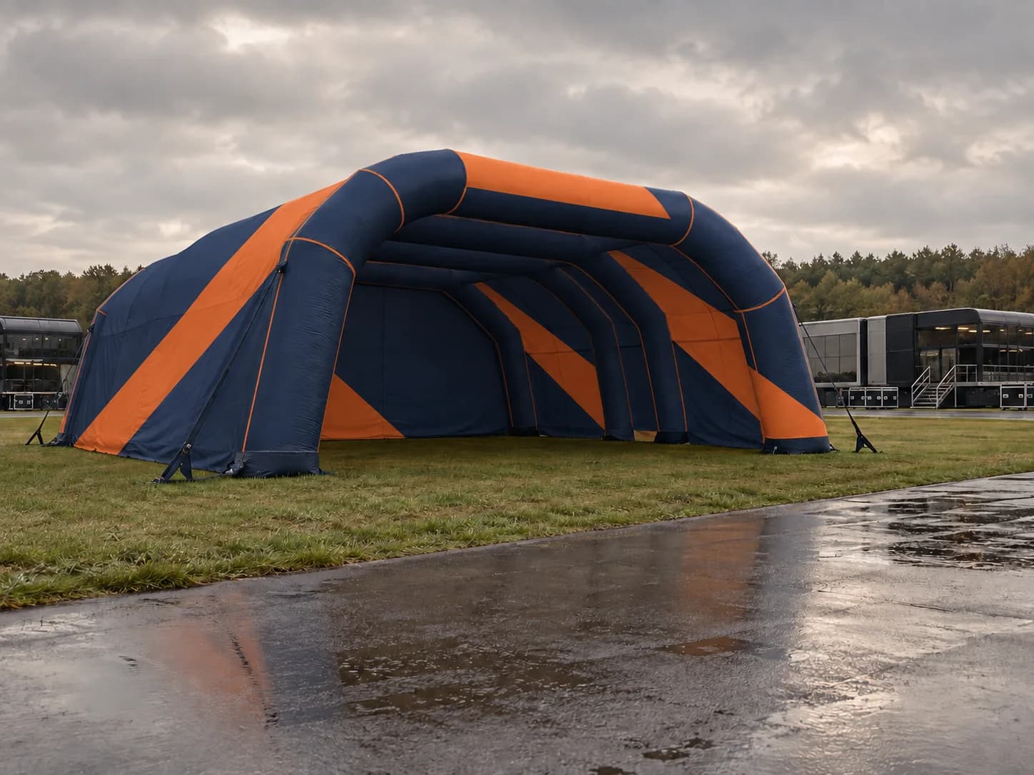 A navy and orange inflatable event structure on grass beside a wet paddock.